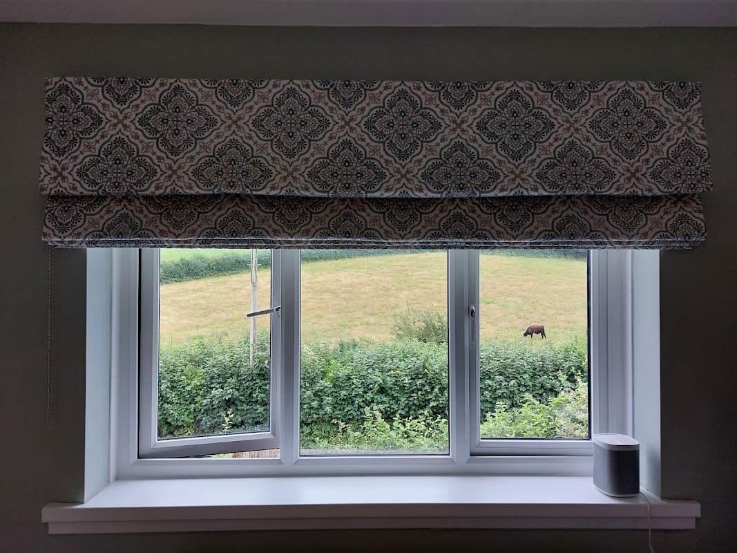 Stylish patterned window valance above a view of green fields and a grazing horse outside.