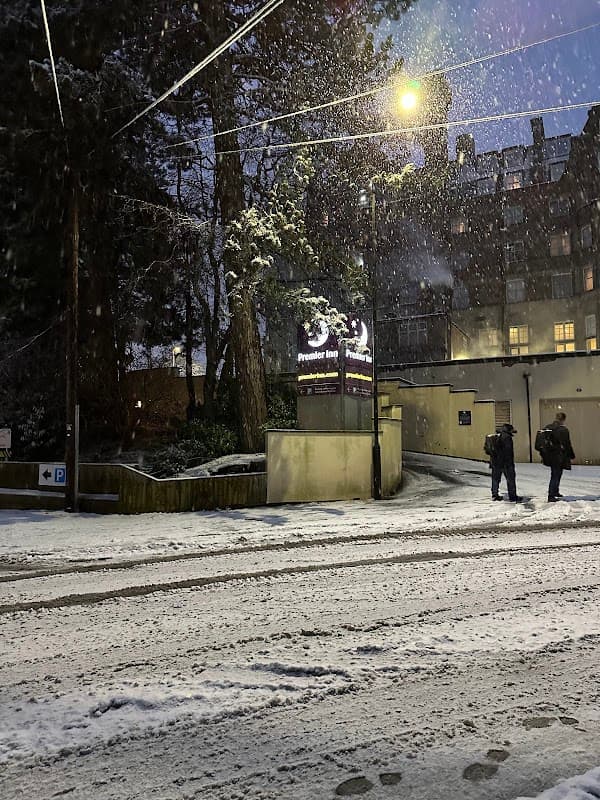 Snow-covered ground with two people walking, streetlights illuminating a multi-storey car park entrance in Harrogate.