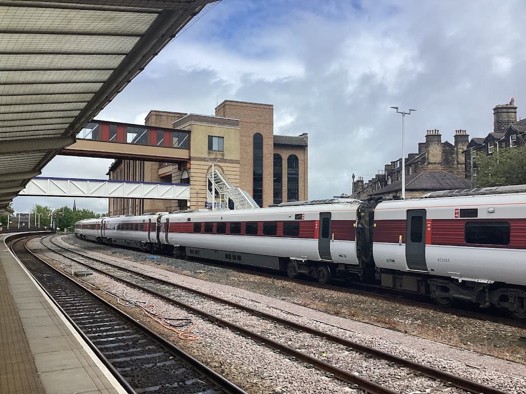 Train tracks with parked trains at Harrogate station, surrounded by modern and traditional buildings under a cloudy sky.