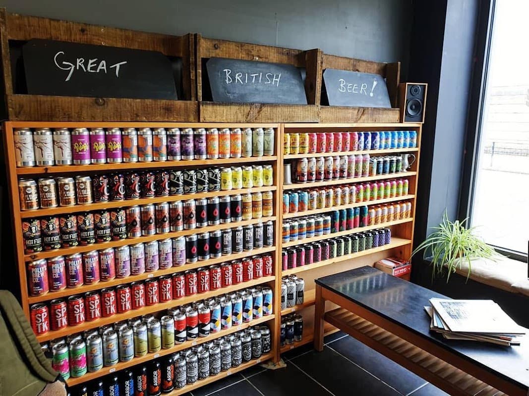 Colorful shelves filled with various beer cans, chalkboard signs reading "Great British Beer!" and a wooden table nearby.