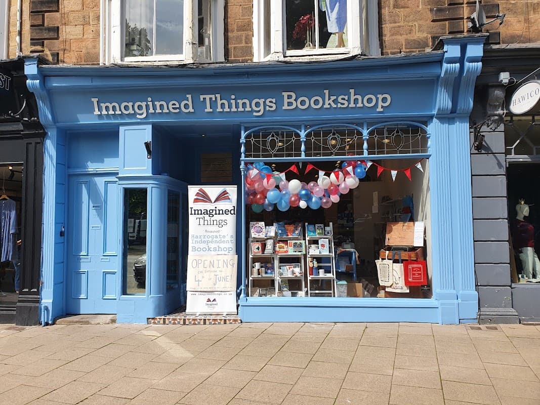 Bright blue storefront with "Imagined Things Bookshop" sign, colorful balloons, bunting, and a display of books.