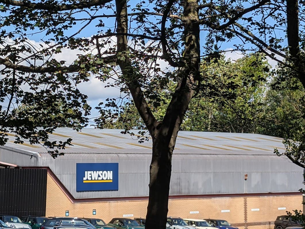 Jewson building with large blue sign, surrounded by trees and a parking area with cars in Harrogate, Yorkshire.