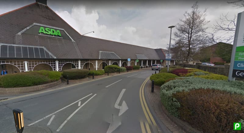 Pay & Display parking area near Asda, featuring landscaped shrubs and trees, with signage indicating parking rules.