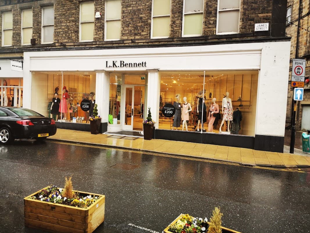 L.K. Bennett storefront with large windows displaying colorful clothing, mannequins, and a rainy street scene.