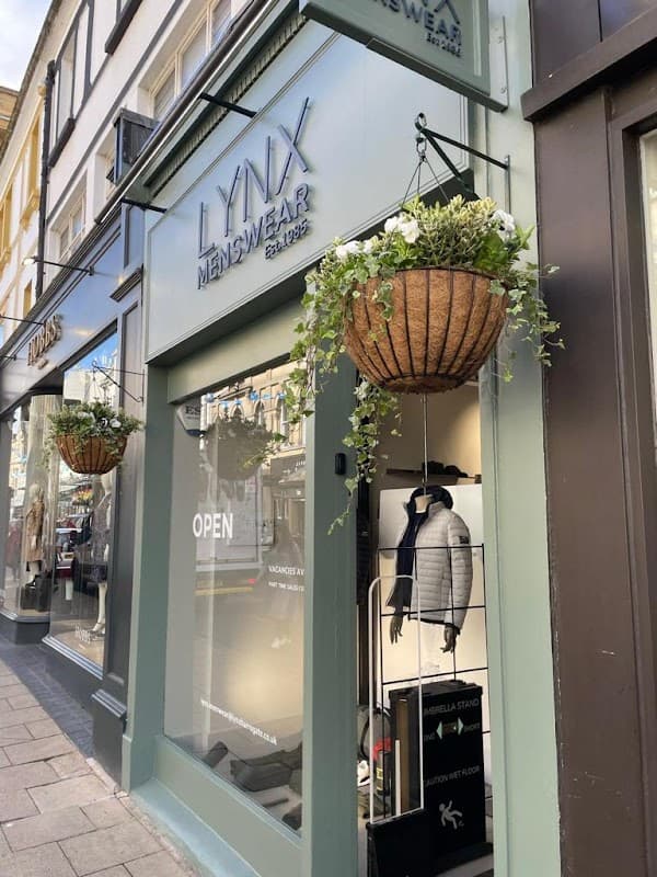 Lynx Menswear shopfront with hanging flower baskets, open sign, and stylish men's clothing displayed inside.