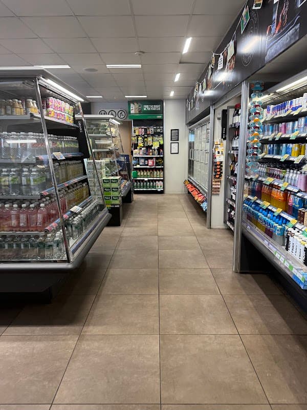 A well-lit corner shop aisle with shelves stocked with drinks, snacks, and convenience items.