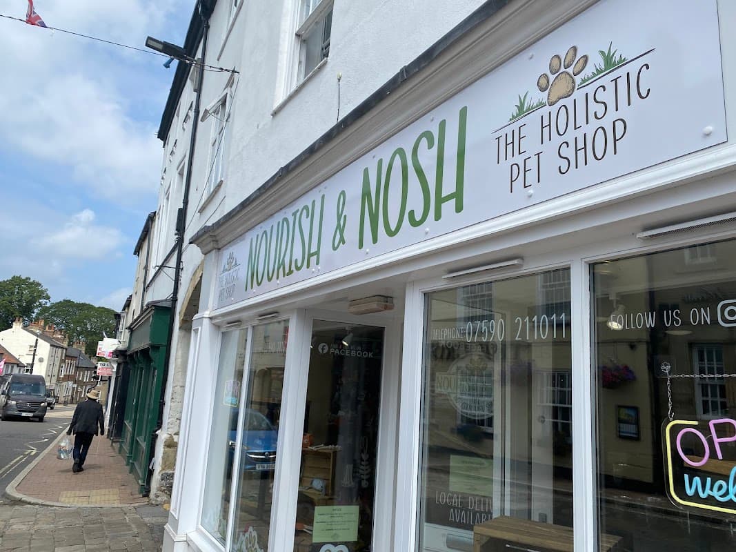 Sign for "Nourish & Nosh", a holistic pet shop, with a paw print logo, located in a charming street in Harrogate.