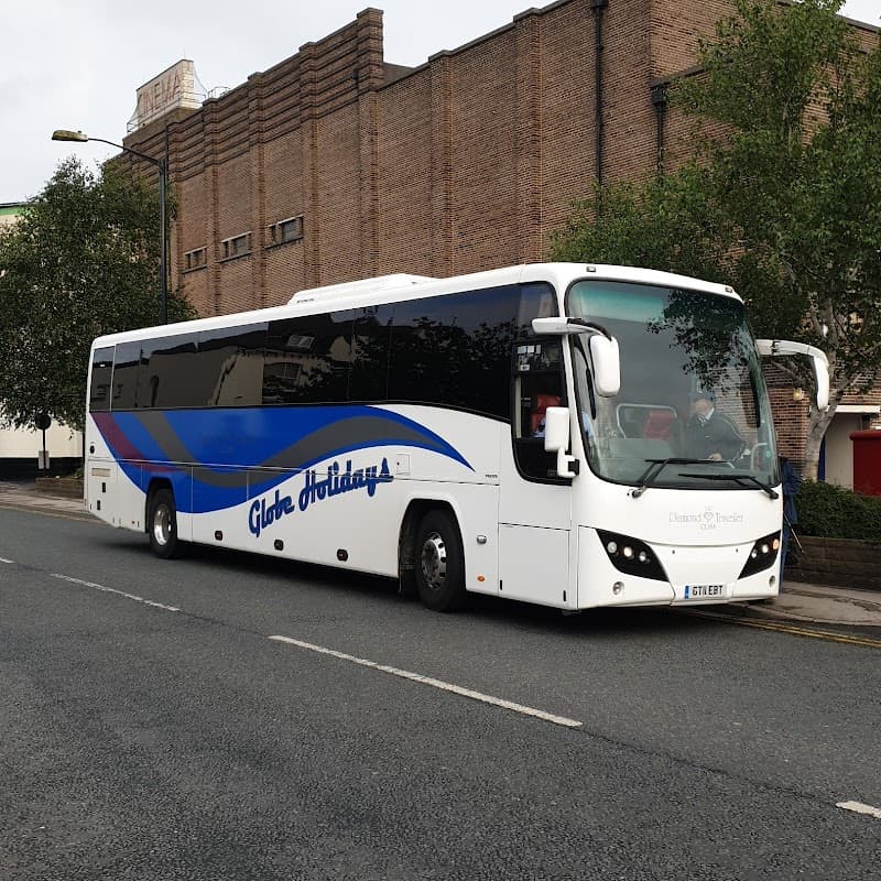 A large white coach with blue accents parked on a street near a brick building, surrounded by trees.