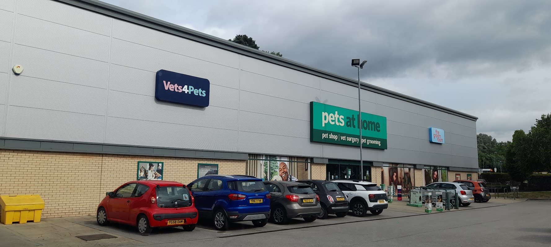 Exterior of Pets at Home shop in Harrogate, featuring a row of parked cars and cloudy skies.