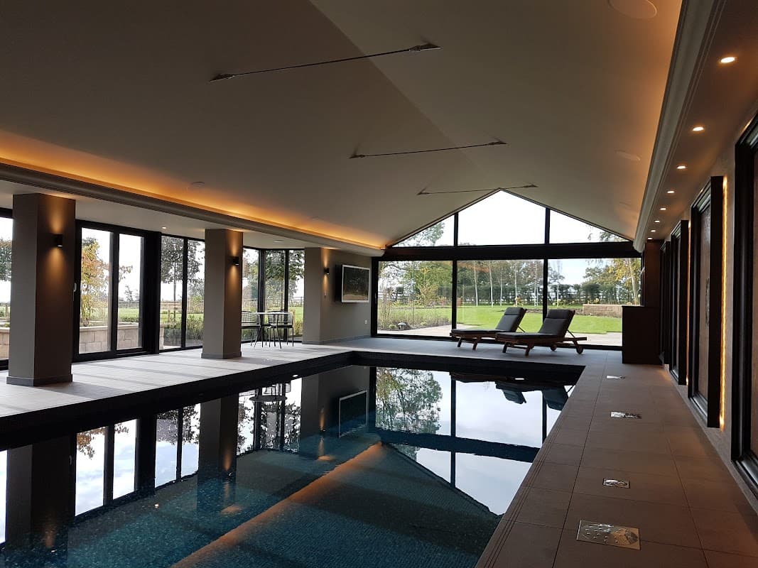 Modern indoor pool area with large windows, sleek lighting, and lounge chairs overlooking a scenic outdoor view.