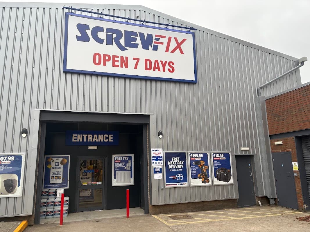 Screwfix store exterior with large sign, entrance doors, and promotional banners on a gray building.