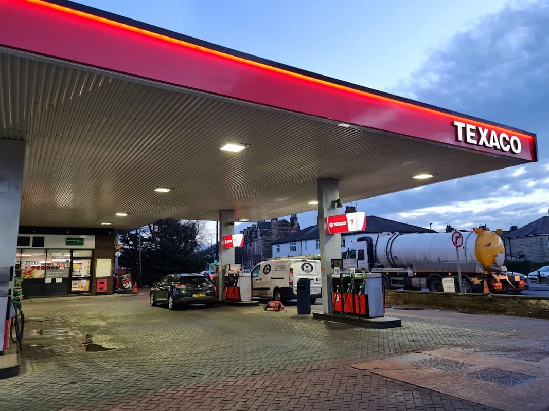 Texaco garage with fuel pumps, a delivery truck, and a convenience store in Harrogate, Yorkshire, under a cloudy sky.