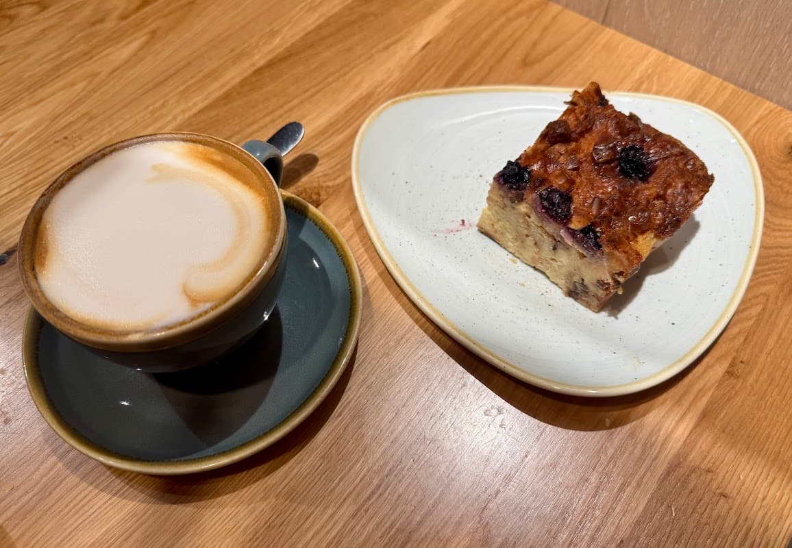 Coffee in a dark cup next to a slice of fruit-topped cake on a plate, set on a wooden table.
