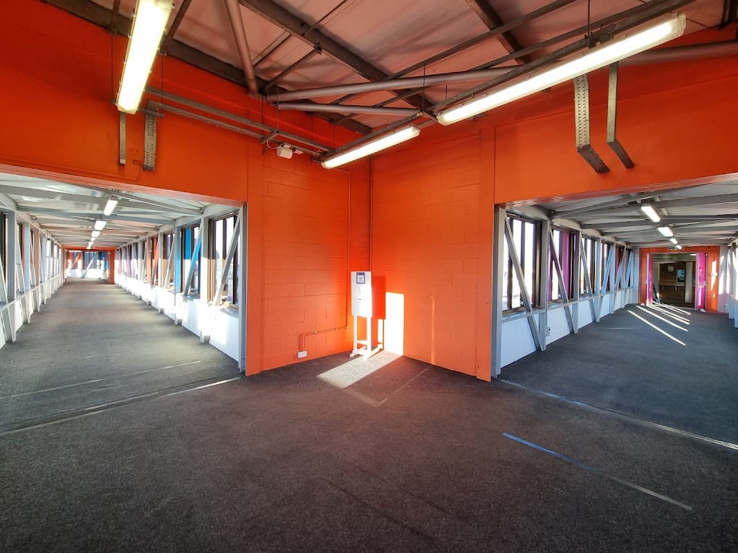Bright orange walls and gray carpet in a multi-storey car park with open walkways and natural light streaming in.