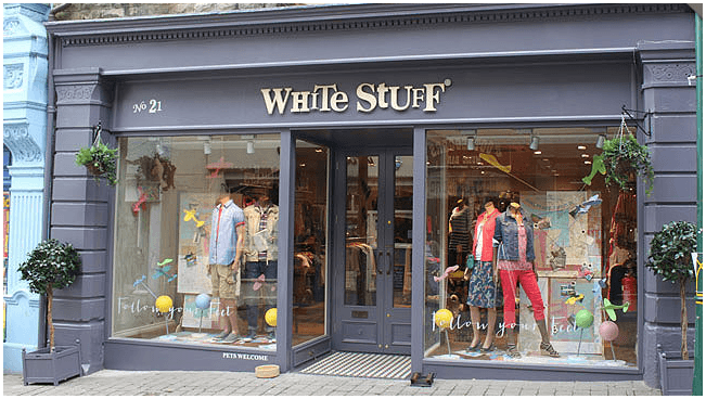 Clothing shop front with mannequins in colorful outfits, large windows, and playful decor elements.