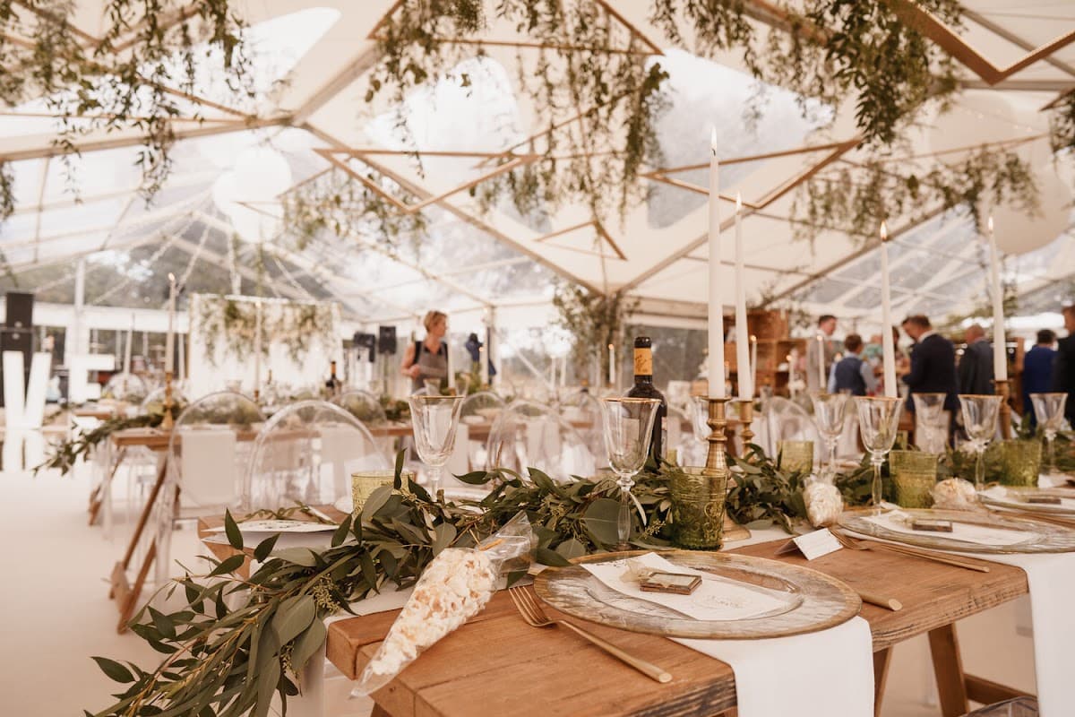 Elegant event setup with long wooden tables, greenery, candles, and a clear marquee, creating a festive atmosphere.