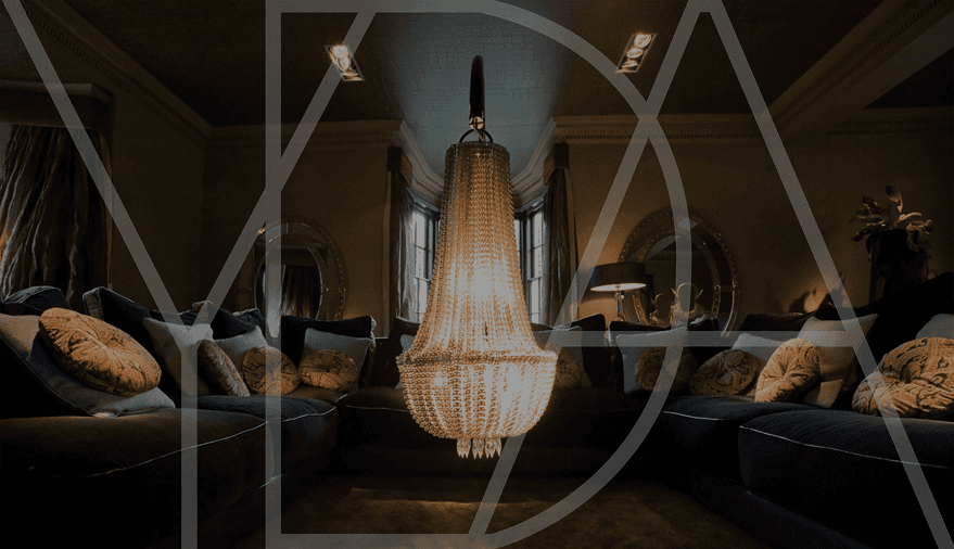 Elegant living room with a grand chandelier, plush sofas adorned with decorative cushions, and stylish lighting.