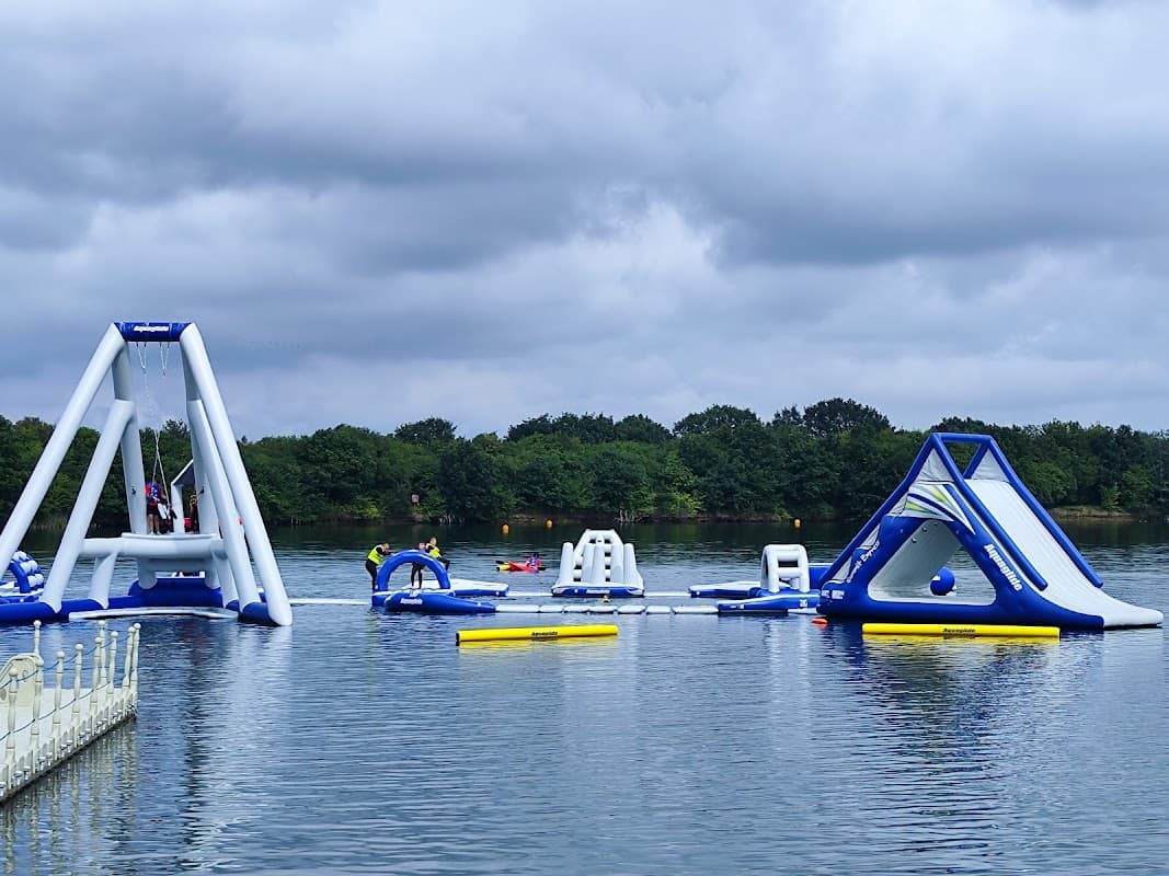 Inflatable water attractions on a lake with cloudy skies and trees in the background.