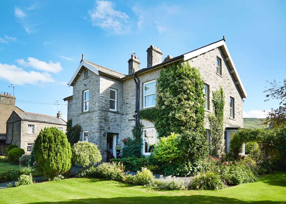 Victorian stone house with ivy, surrounded by a lush garden and bright blue sky in Hawes, Yorkshire.