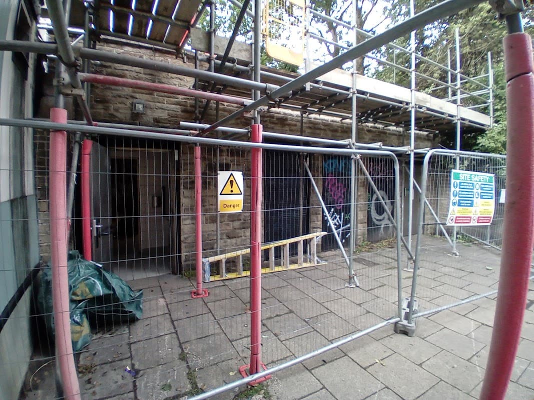 Scaffolding surrounds a stone building with a "Danger" sign and a safety notice, indicating ongoing construction.