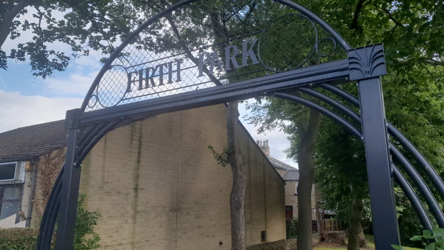 Firth Park entrance archway with trees and a building in the background, set in a green play area.