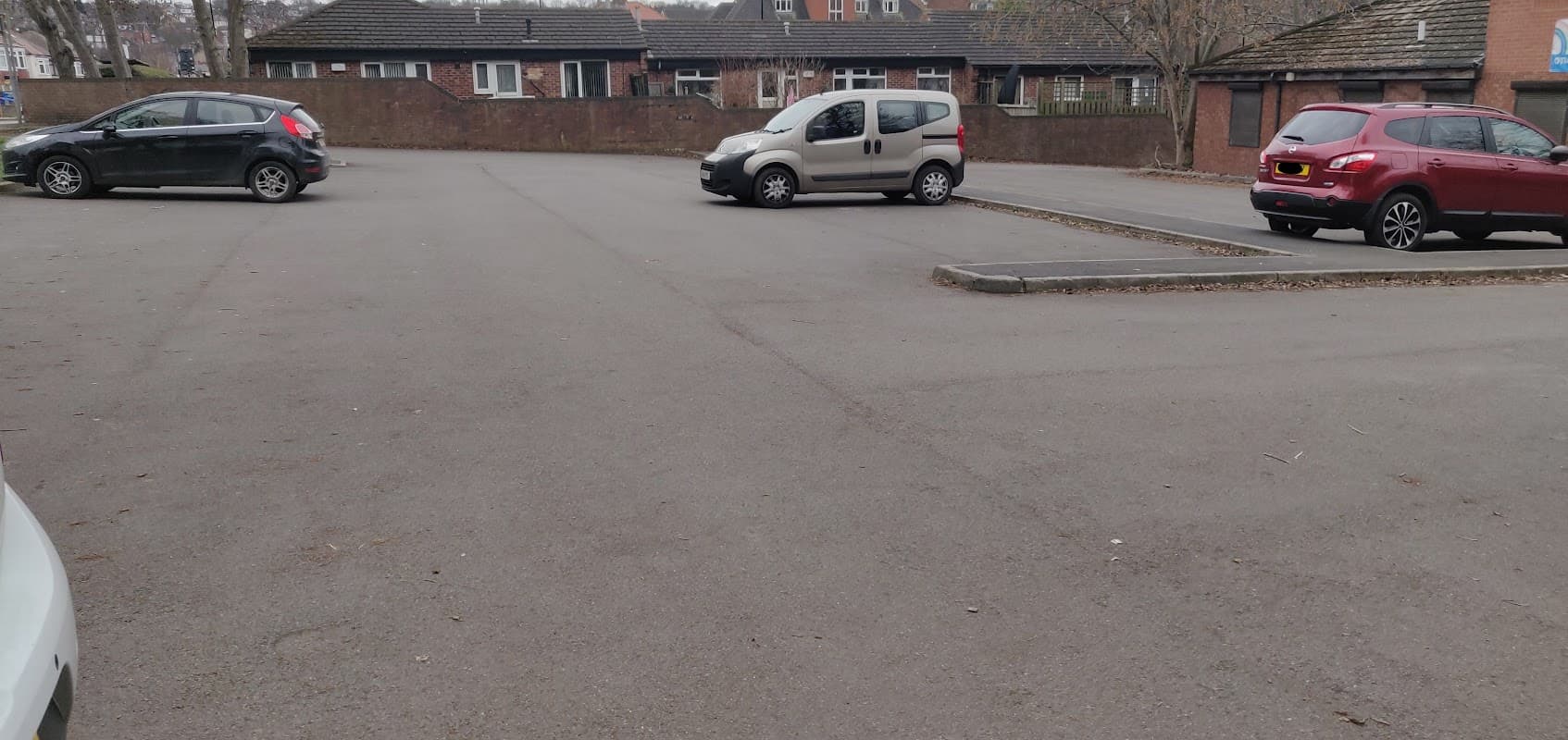 Empty car park with a few parked cars and surrounding buildings in a residential area.
