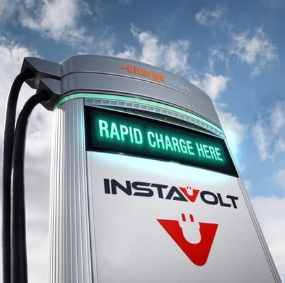 InstaVolt charging station with illuminated sign reading "RAPID CHARGE HERE" against a cloudy sky.