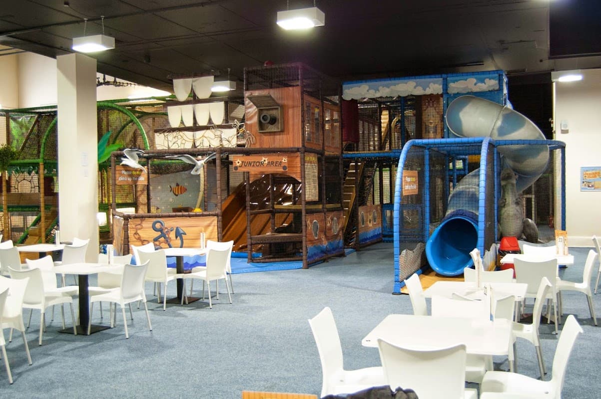 Indoor play area with climbing structures, slides, and seating for diners in a spacious, colorful environment.