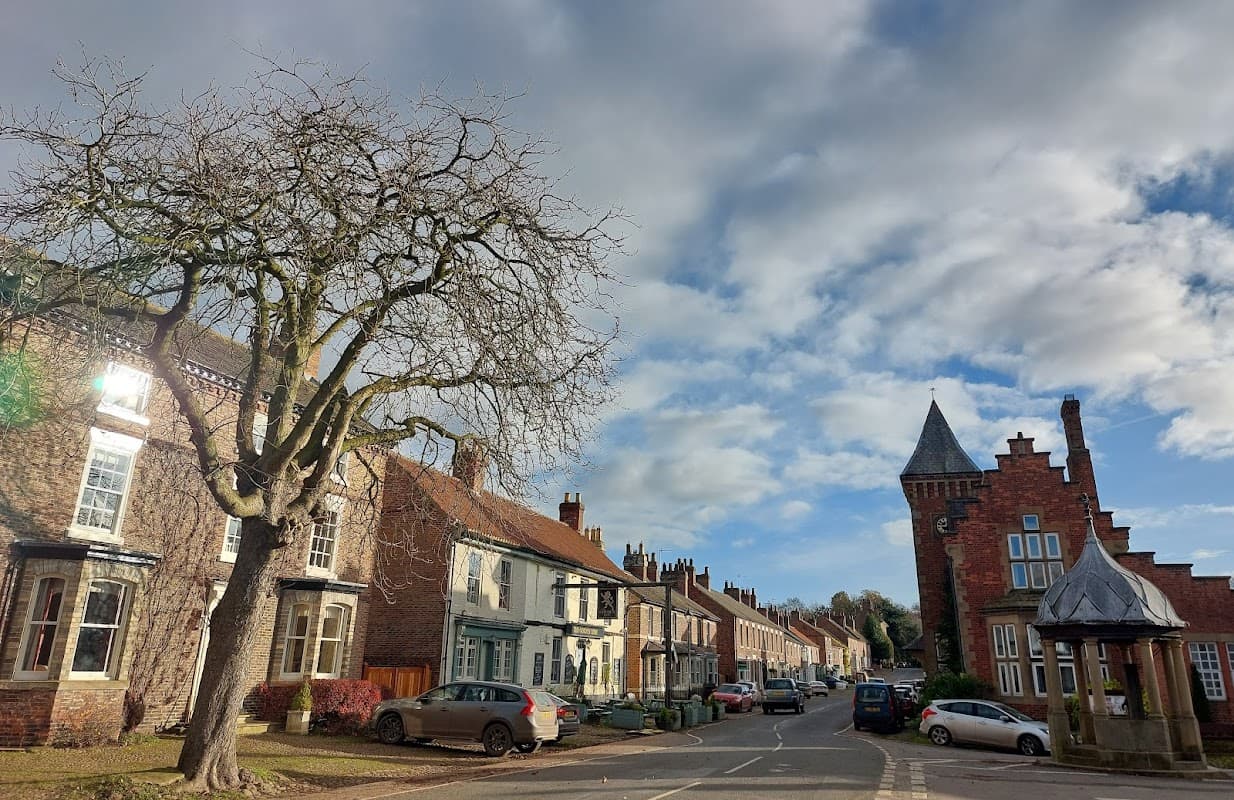 Helperby Village Hall with a tree, traditional houses, and a tower in a quaint Yorkshire village setting.