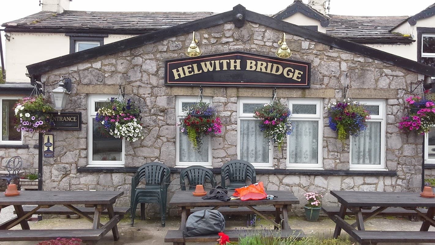 Stone facade of Helwith Bridge Inn with flower baskets, outdoor seating, and a welcoming entrance sign.