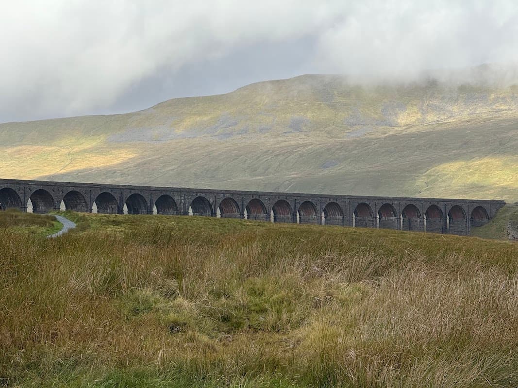 Viaduct spanning a valley, surrounded by grassy hills and misty clouds in Yorkshire Dales National Park.