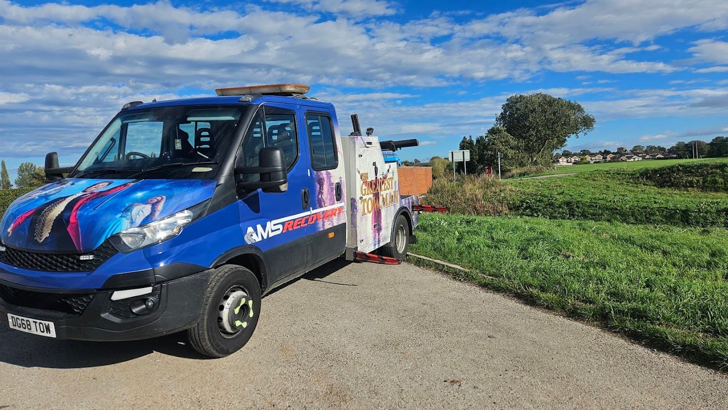 AMS Recovery LTD truck parked on a rural road, featuring colorful graphics, with fields and trees in the background.