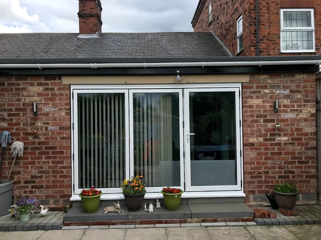 Brick building with sliding glass doors, potted plants, and a patio area. Cloudy sky in the background.