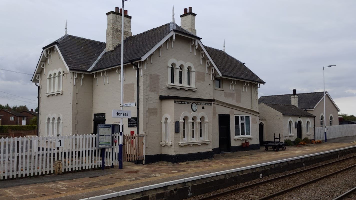 Victorian-style railway station building in Hensall, North Yorkshire, with a white picket fence and platform.