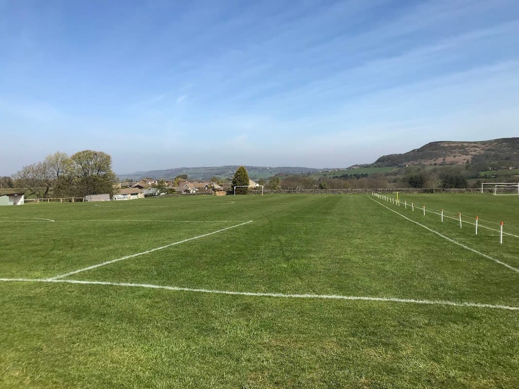 Green football pitch with goalposts, surrounded by trees and hills under a clear blue sky in Hepworth, Yorkshire.