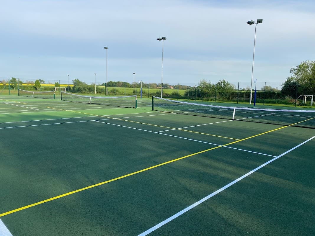 Tennis courts with nets and markings, surrounded by greenery and a clear sky at Stamford Bridge Tennis Club.