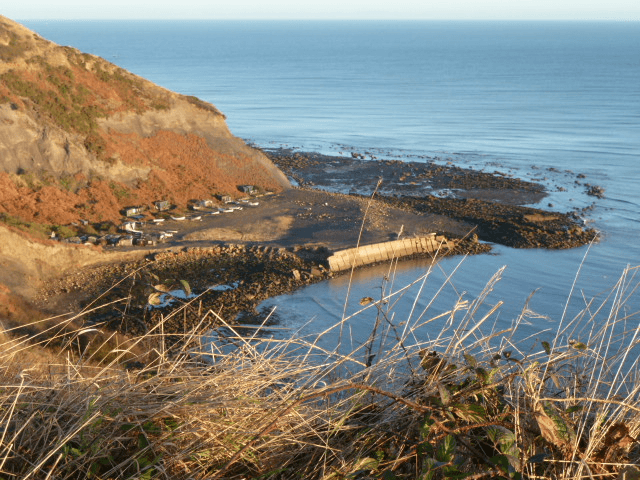 Coastal view of Hinderwell with rocky shoreline, calm sea, and distant cottages nestled among the cliffs.