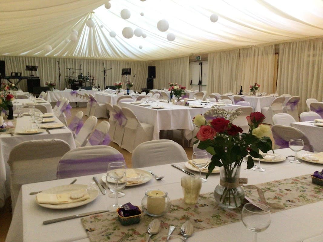 Elegant dining setup with tables adorned in white linens, purple accents, floral centerpieces, and soft lighting.