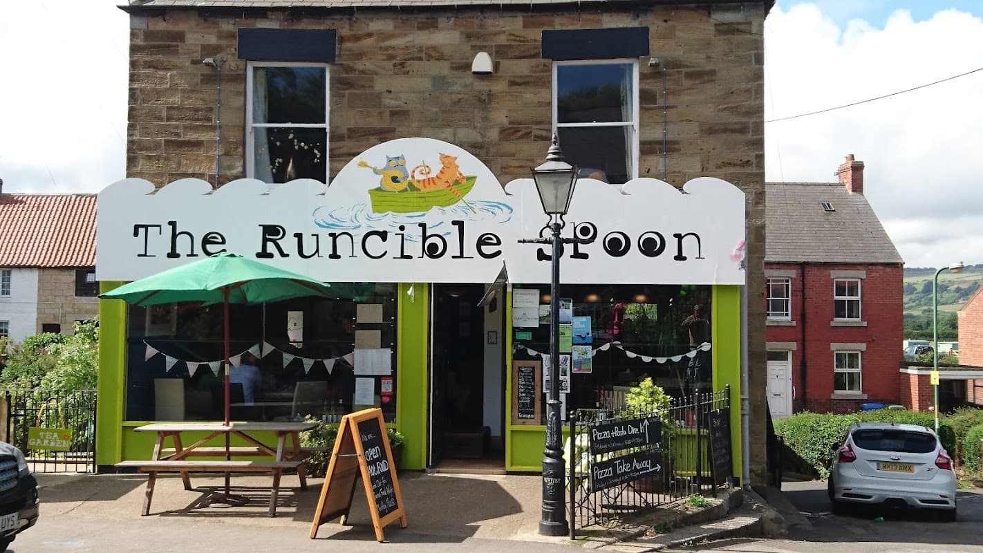 The Runcible Spoon café features a colorful sign, outdoor seating, and a green façade in Hinderwell, Yorkshire.