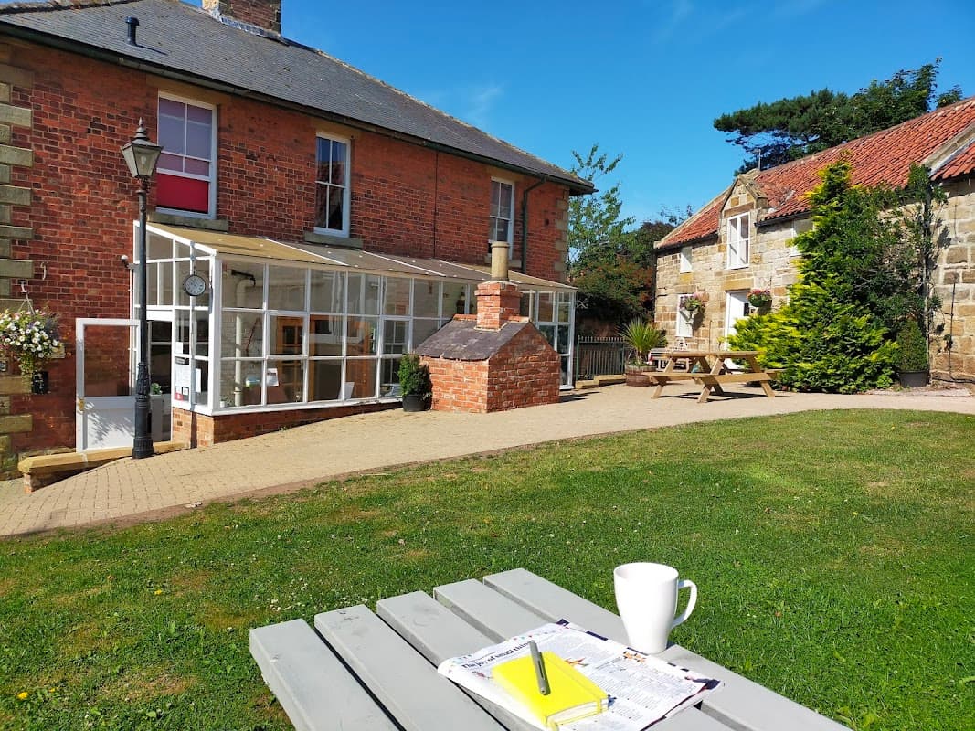 Charming boutique hotel with a red brick exterior, outdoor seating, and a sunny garden area in Hinderwell, Yorkshire.