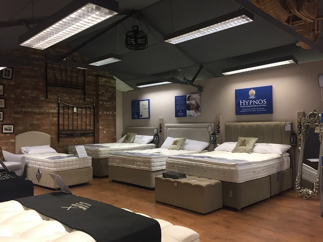 Showroom featuring various stylish beds and mattresses, with a brick wall backdrop and modern lighting.