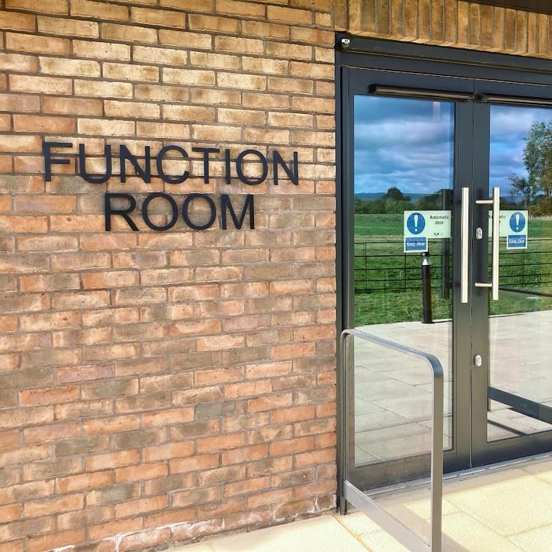 Sign for "Function Room" on a brick wall with glass doors, overlooking green fields in Holme, North Yorkshire.