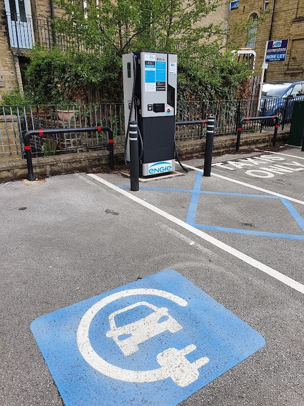 GeniePoint Charging Station with a blue EV charging symbol on the ground, surrounded by greenery and parked vehicles.