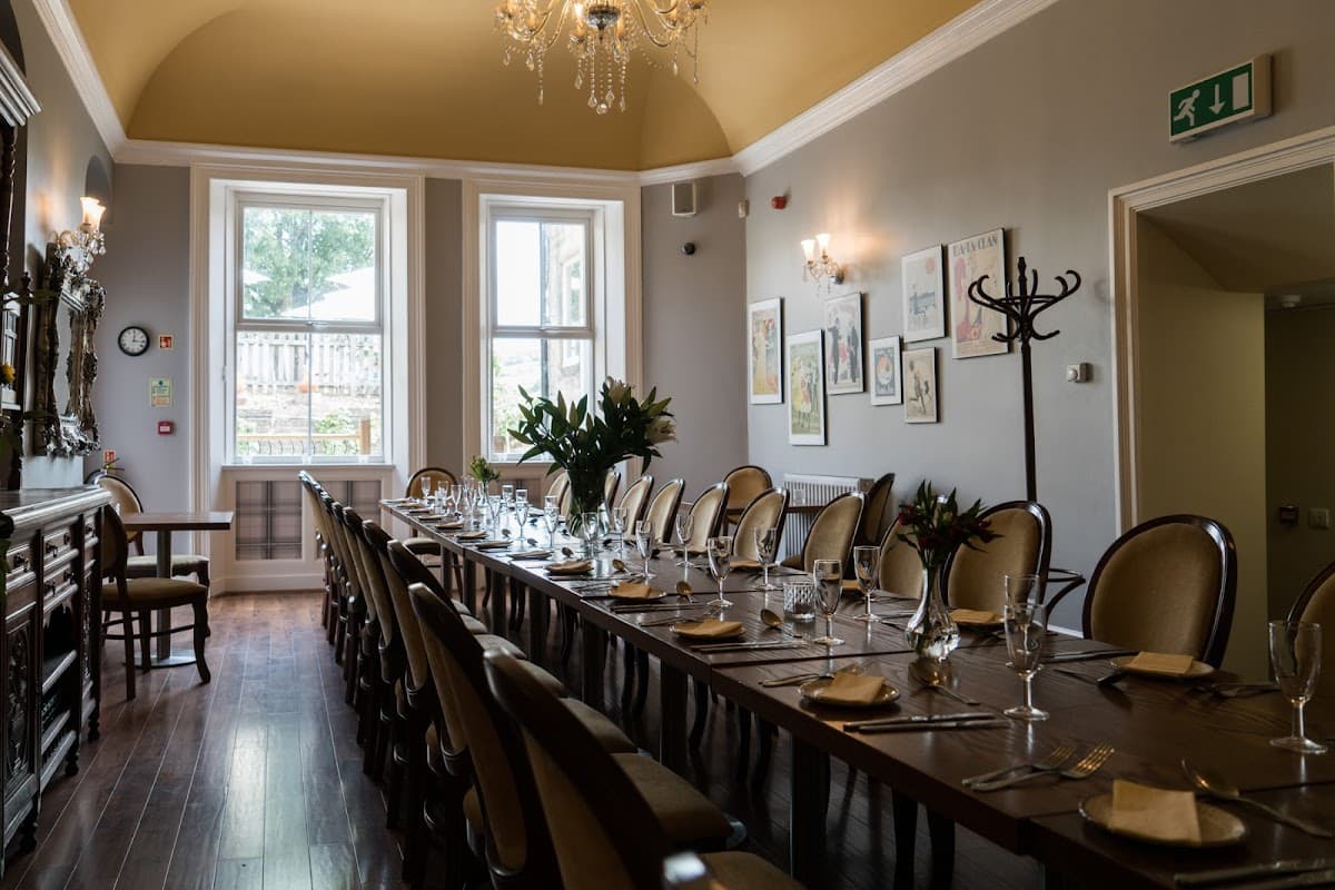 Elegant dining room with a long table set for a meal, large windows, and decorative plants in a cozy bar setting.