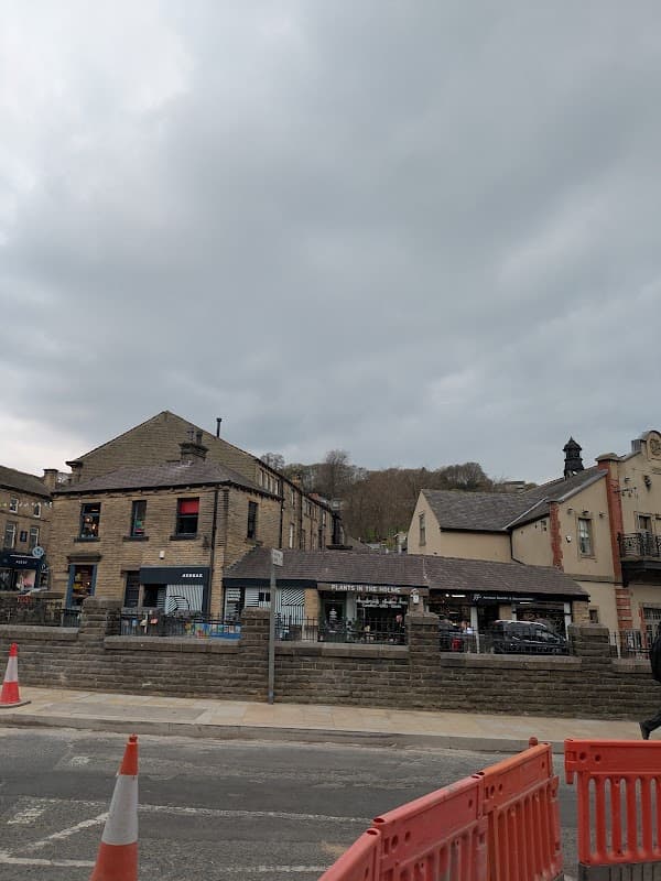 Towngate Car Park in Holme Valley, featuring stone buildings, shops, and a cloudy sky above. Traffic cones in the foreground.