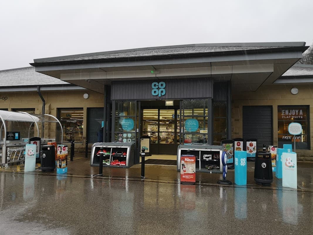 Co-op Food store entrance with shopping carts, outdoor displays, and a rainy atmosphere in Holmfirth, Yorkshire.