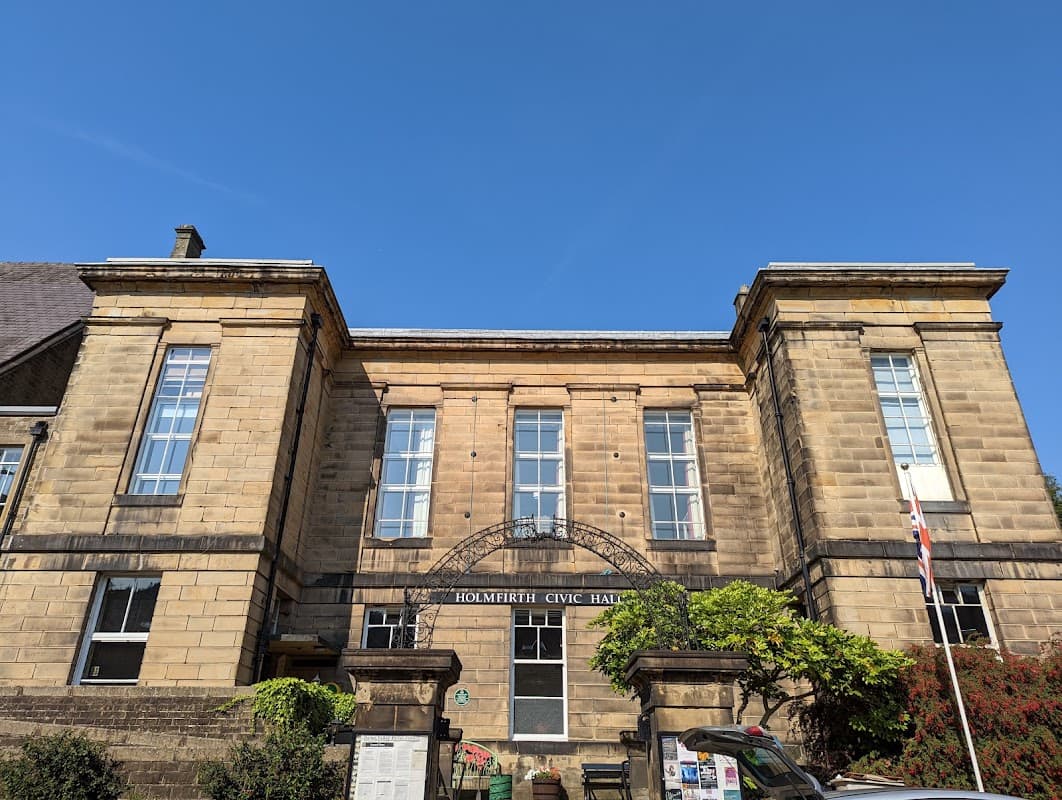 Historic stone building with large windows, greenery, and a flag, set against a clear blue sky.