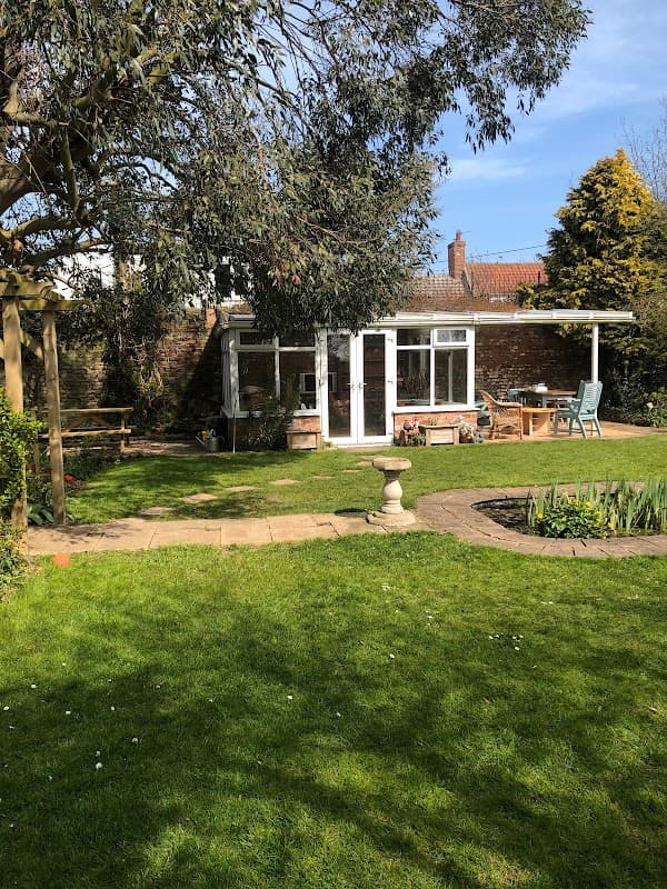 Charming garden at Elm Tree Farm B&B with green lawn, seating area, and a small patio surrounded by trees.