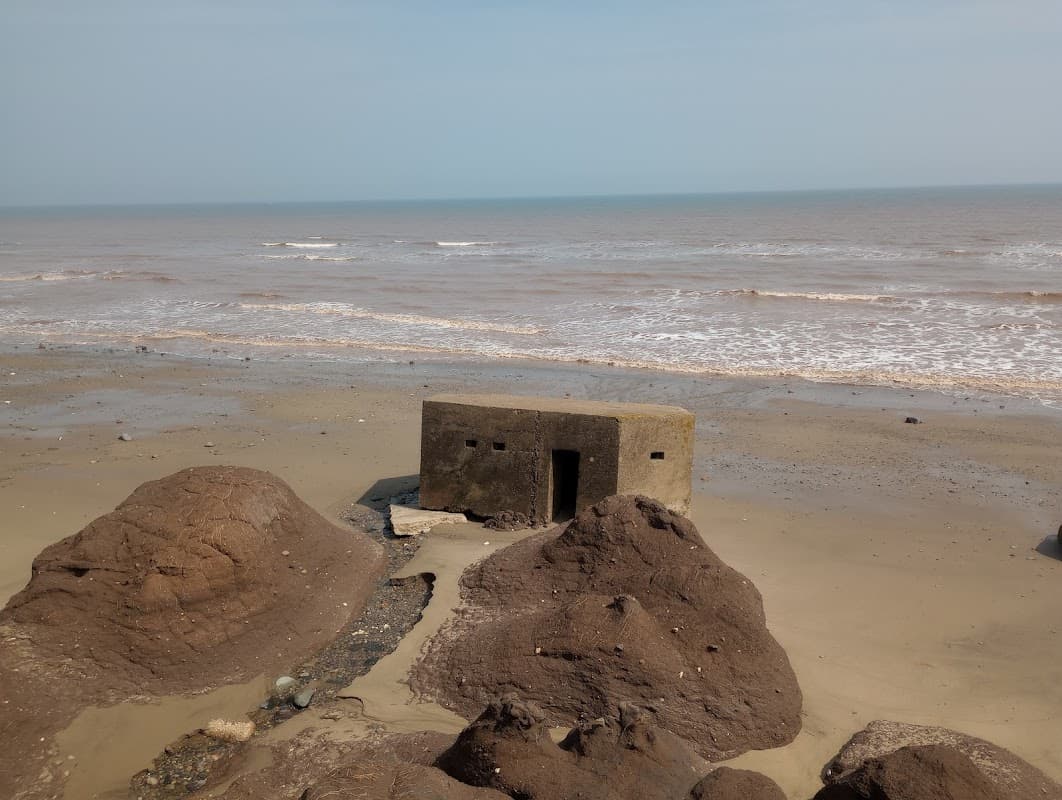 A weathered concrete structure on a sandy beach, with waves lapping at the shore and rocky formations nearby.