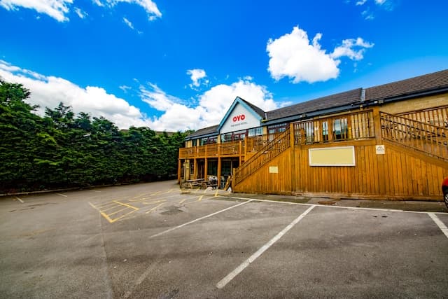 OYO The Rock Hotel with wooden deck, surrounded by greenery and a clear blue sky, in Holywell Green, Yorkshire.